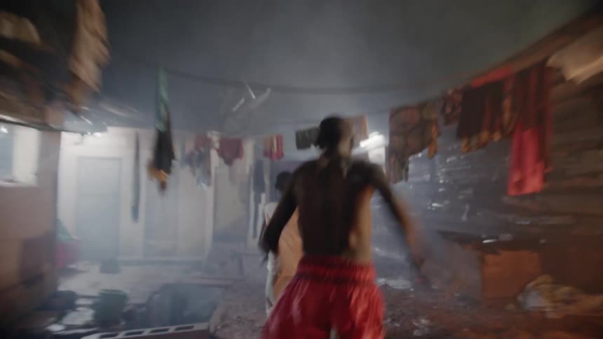 Two people run frantically through a building with clothes hanging all around