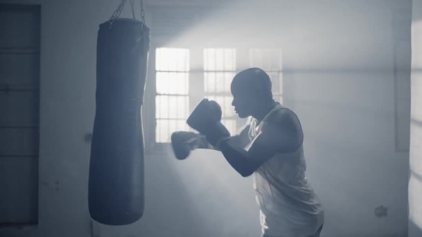 A man punches the heavy bag in the dark gym