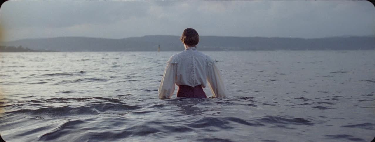 Woman walks into the water under a cloudy sky