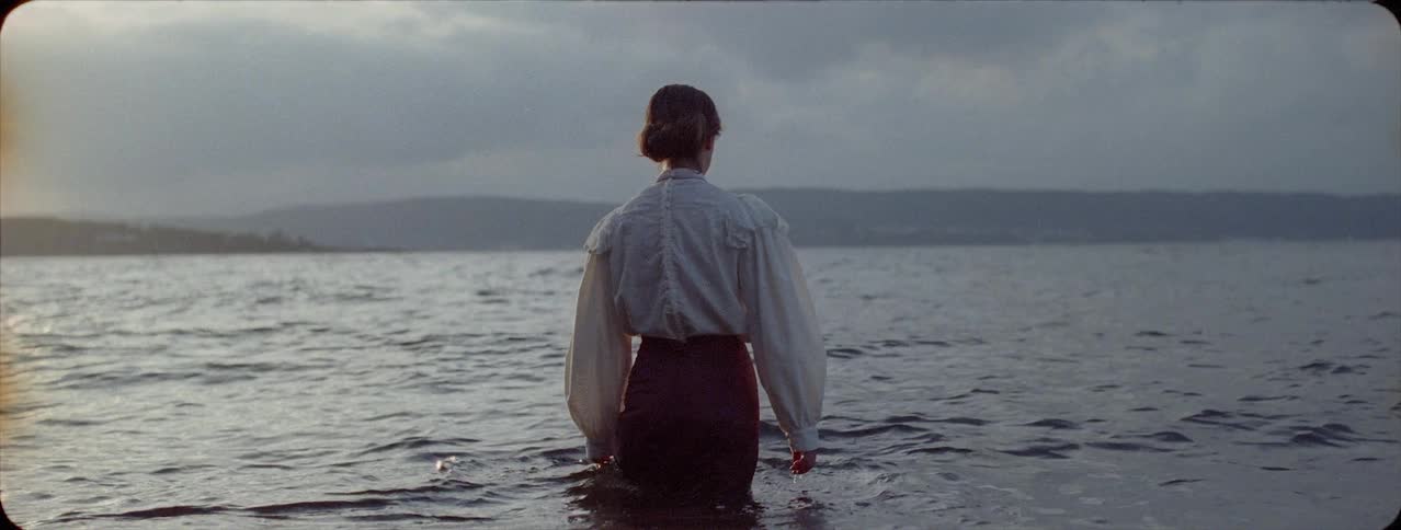 Woman is wading into lake water in dress on cloudy day