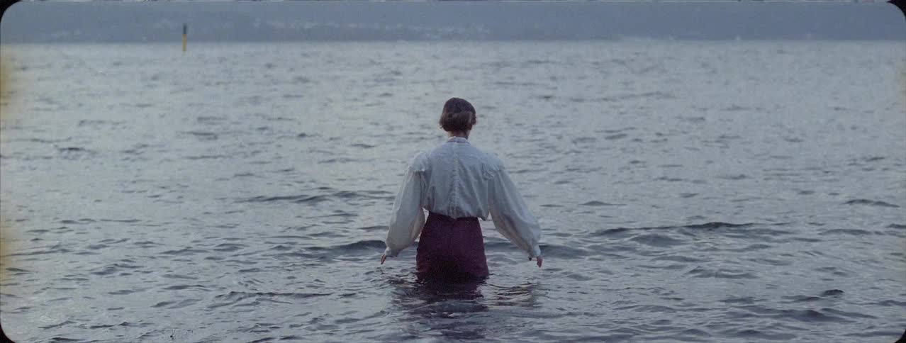 Woman is wading into lake water in a dress