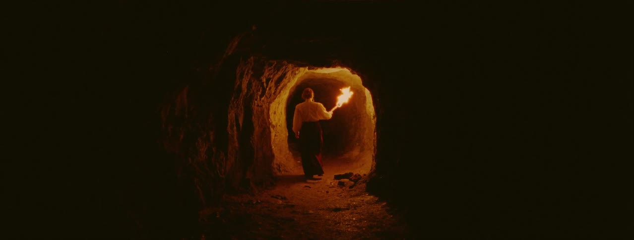 Woman holding fire torch is walking through dark cave
