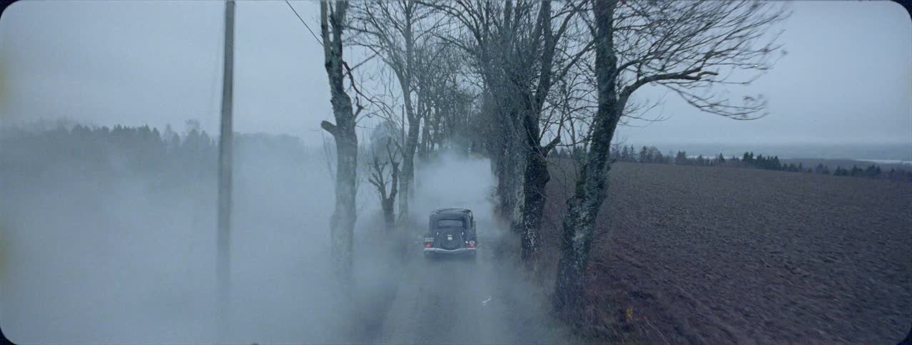 Old car drives away from house and down foggy country road