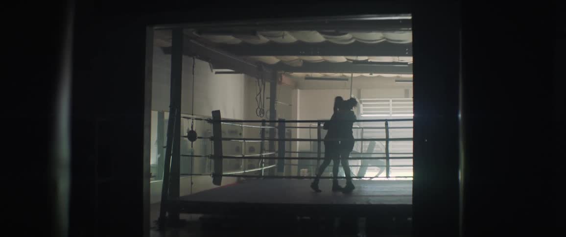 Two women are tapping gloves and hugging inside a boxing ring in daylight