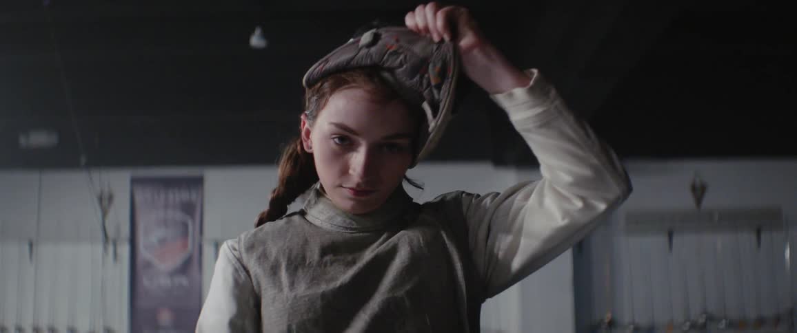 A woman removes her fencing mask