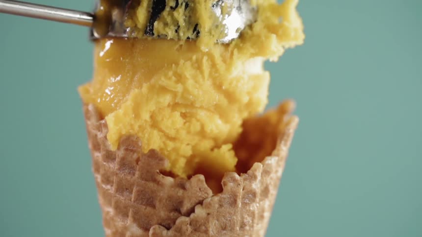 Ice cream scoop puts a ball of yellow ice cream on a cone