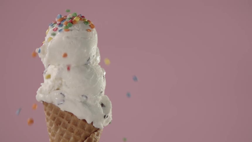 Rainbow sprinkles are dropped on a double scoop waffle cone