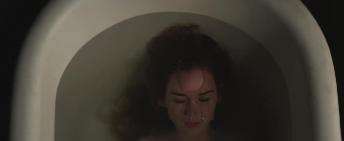A woman lays in a bathtub and lowers her head beneath the water line
