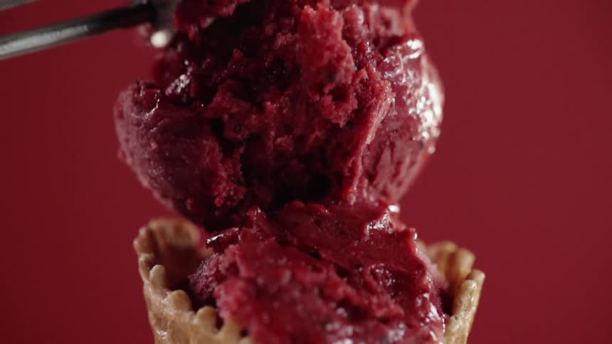 Ice cream scoop puts a scoop of red ice cream on a cone