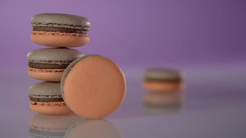 One macaroon rolls across a table and hits into a stack of three macaroons