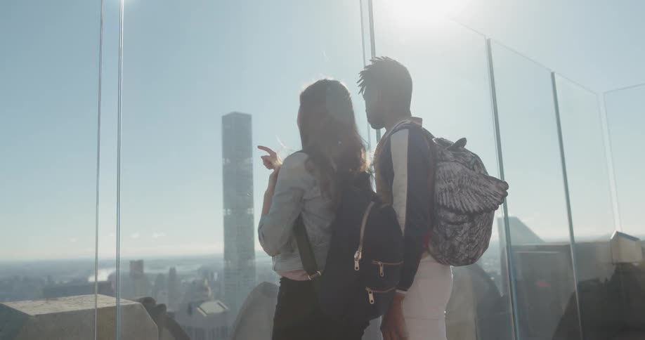 Man and woman sightseeing on top of a large building looking at buildings below