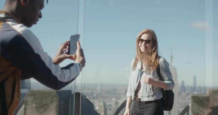 Man takes a picture of a woman while standing on top of a skyscraper