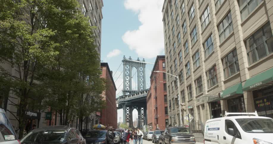People walk down the city street away from the bridge