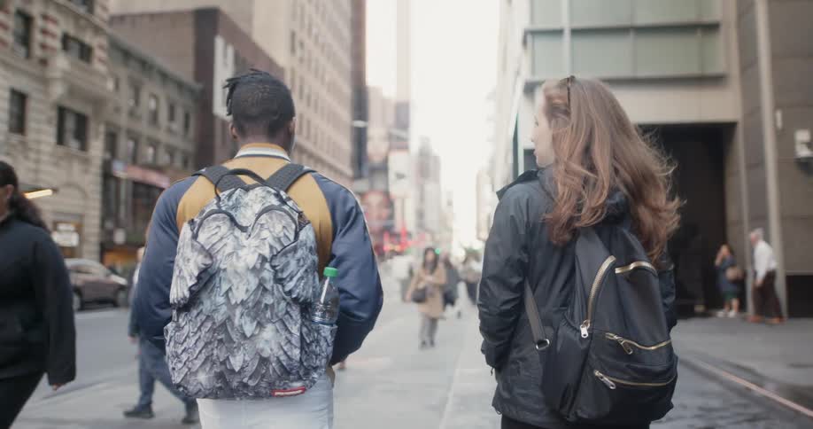 Man and woman wearing backpacks walk down a city sidewalk