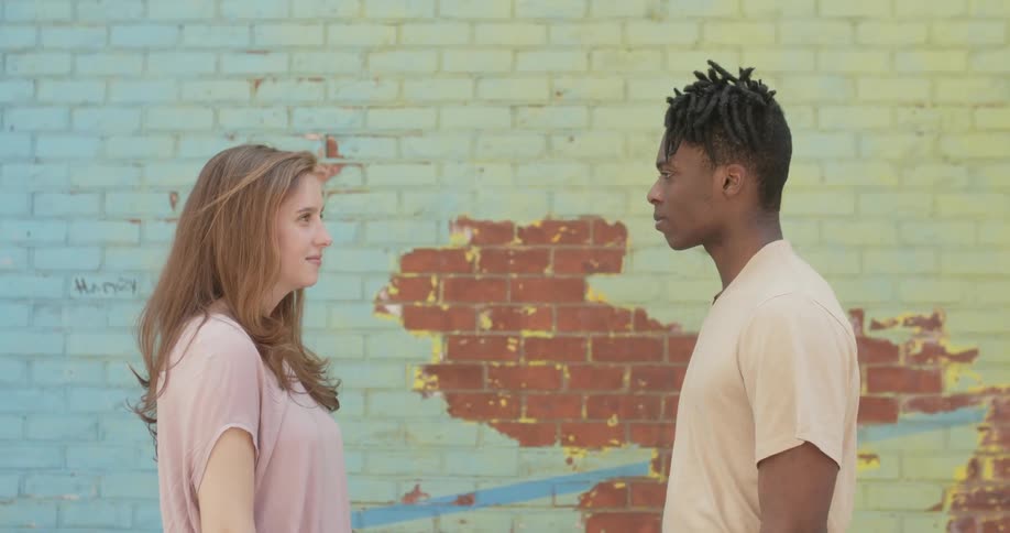 A man and woman face each other in front of a brick wall
