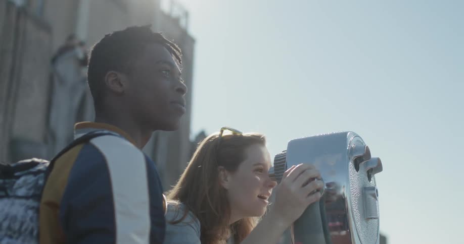 A woman looks through a tower viewer and then lets her friend look through