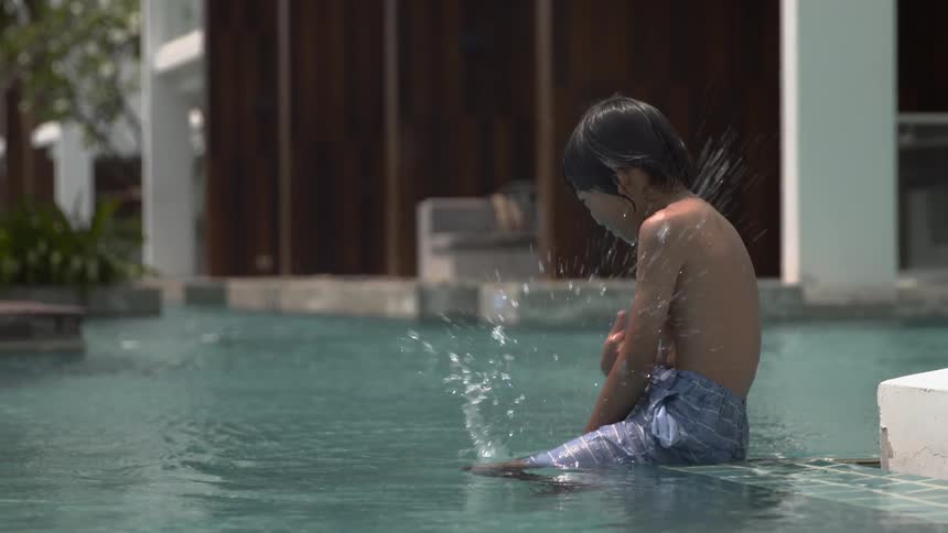 The child is sitting on the edge of the pool kicking the water