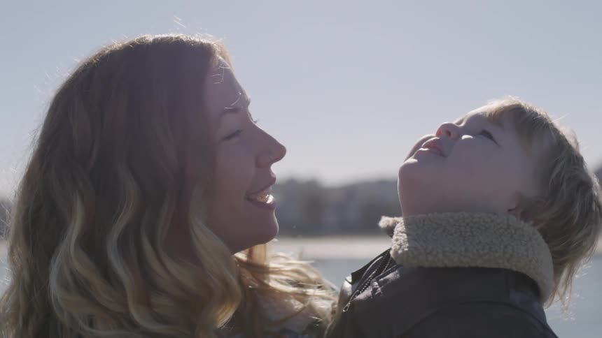 A boy held by his mom points and then looks up to the sky