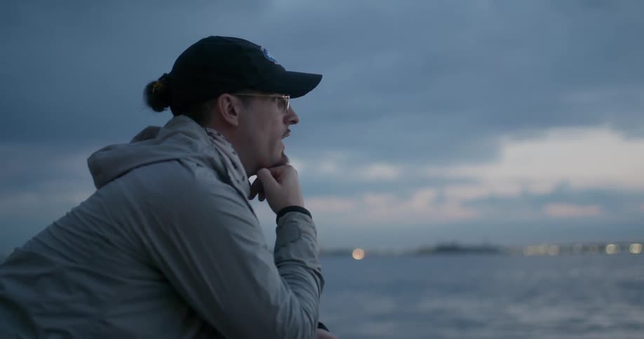 Man leans on railing and looks out over the water
