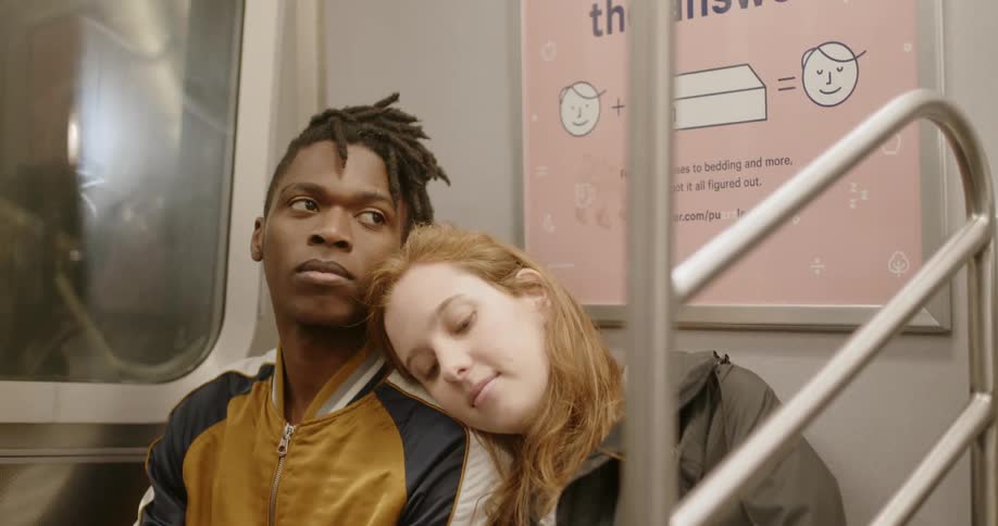 A woman rests on a man's shoulder as they ride the train