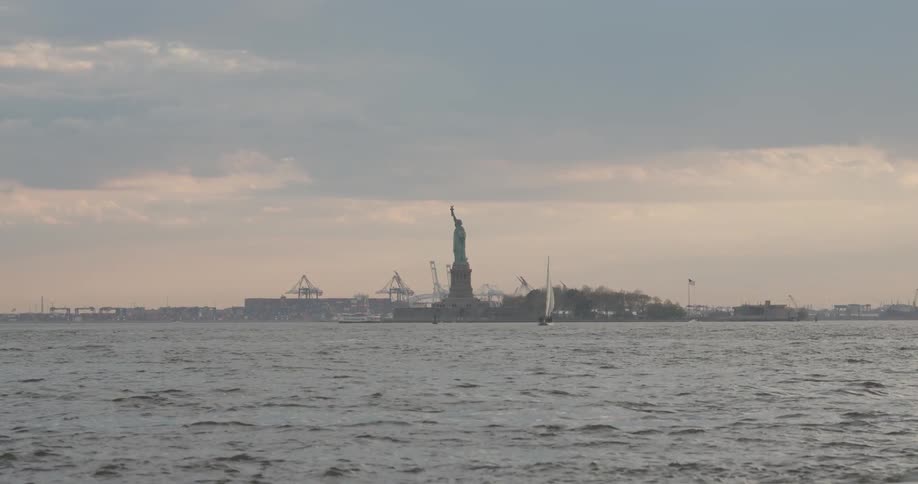 The statue of liberty sits in the distance under heavy clouds