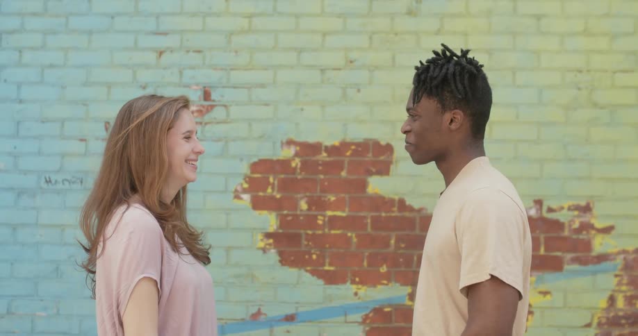 A man and woman laugh and talk near the tall brick wall