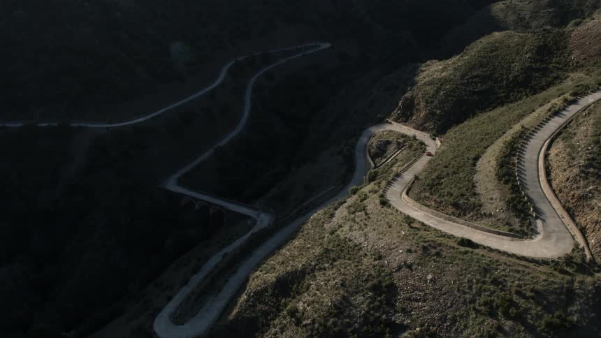 The car drives around the winding roads on the hills