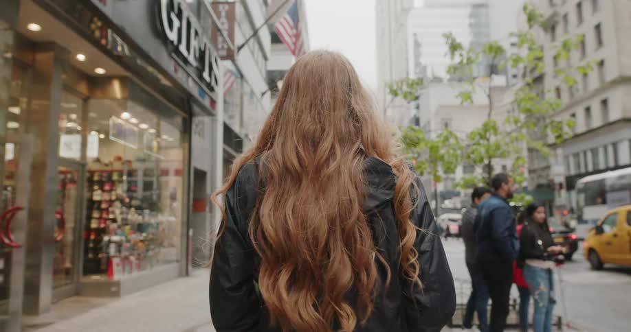 A woman walks down the city street past stores