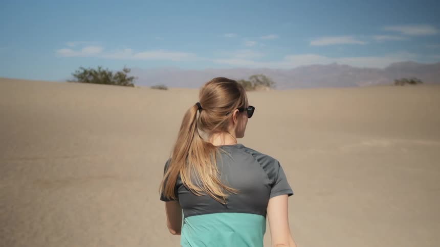 A woman walks in the desert wearing sunglasses
