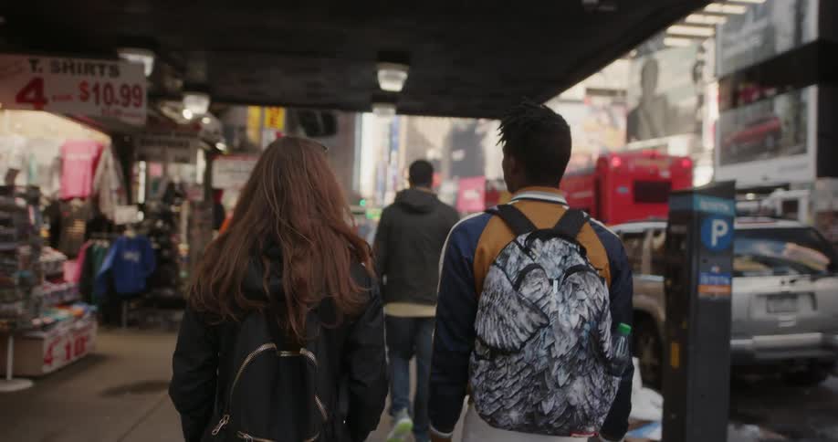 Man and woman walk downtown in a busy city past stores