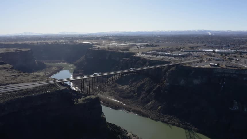 The cars travel over the large bridge over the river