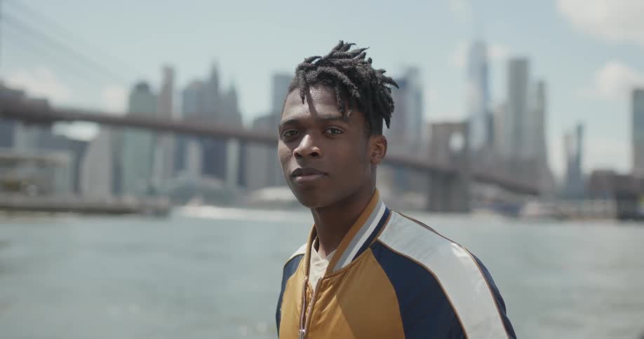 Smiling man stands by a river and a city