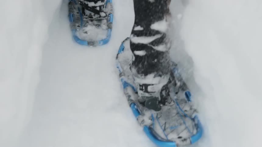 A person is walking in the snow slowly with snowshoes