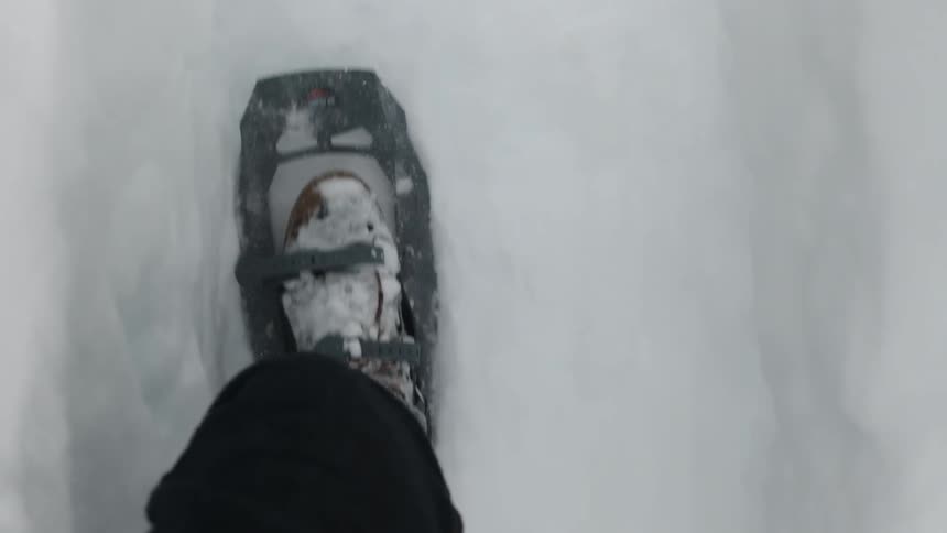 A person kicks the snow in the snow shoes as they walk