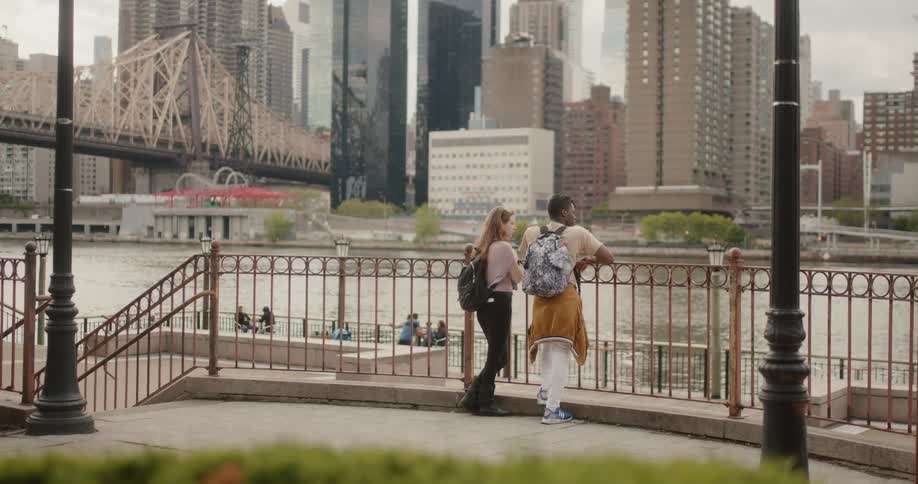 A man and woman lean on a rail and look at the river and city
