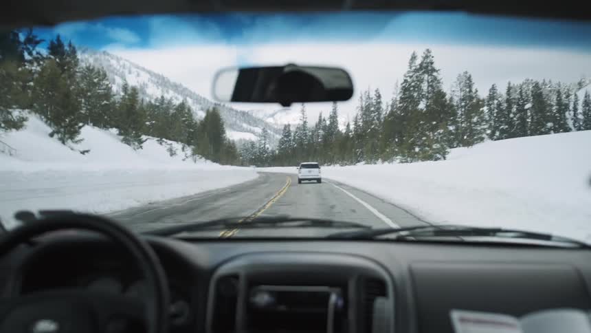 The cars drive past tall piles of snow on the side of the road