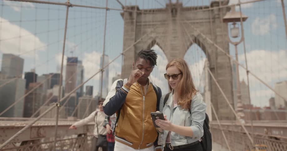 Woman wearing sunglasses looks at her cellphone while a man next to her watches