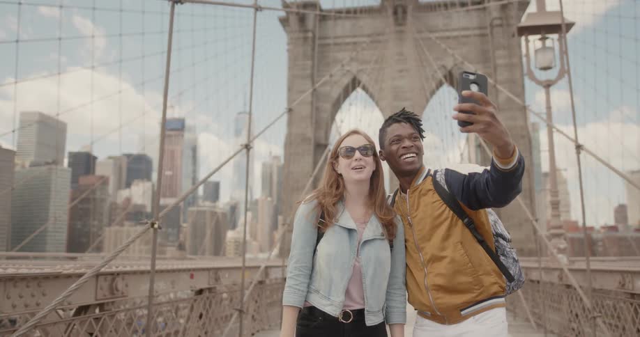A couple takes a selfie on a bridge with a city behind them