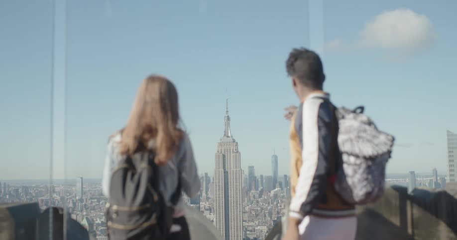 Two people stand on the roof of a tall building watching over the city