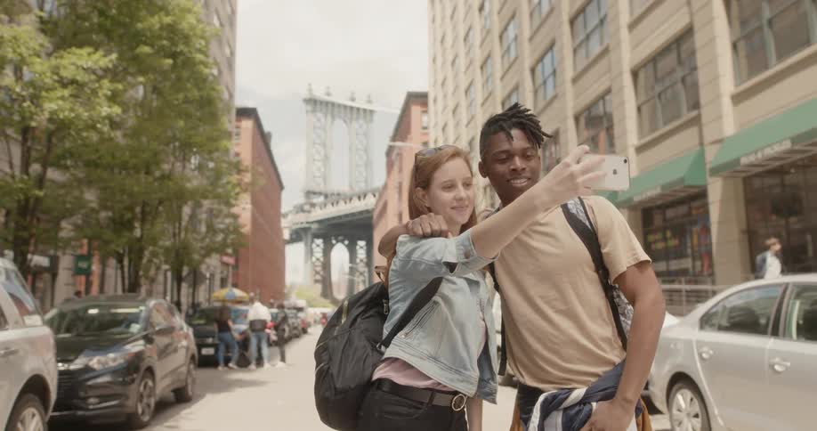 Man and woman stand in the street as the woman takes a photo of them with her cellphone