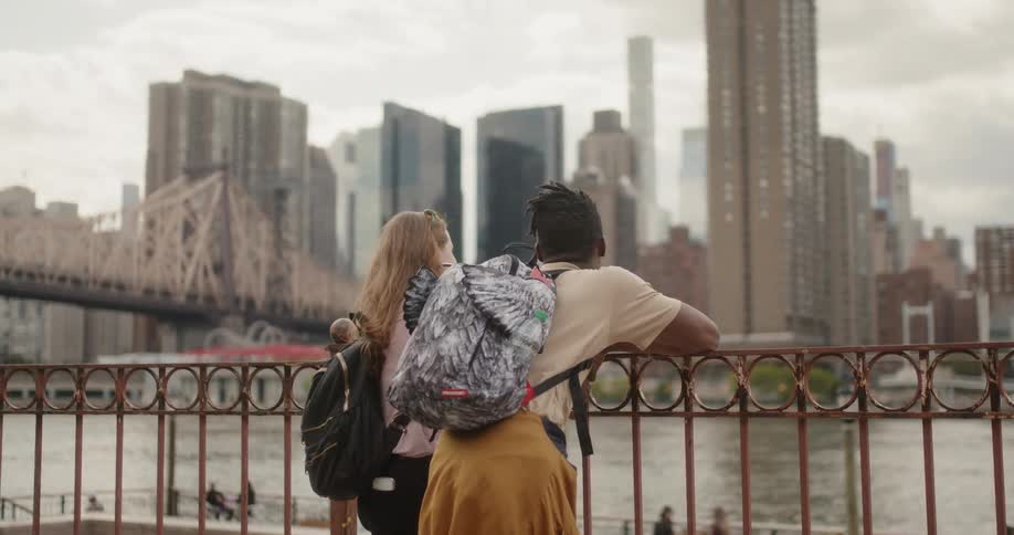 Man and woman lean on railing and look at city river