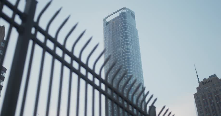 The fence leads to a very tall tower in the city
