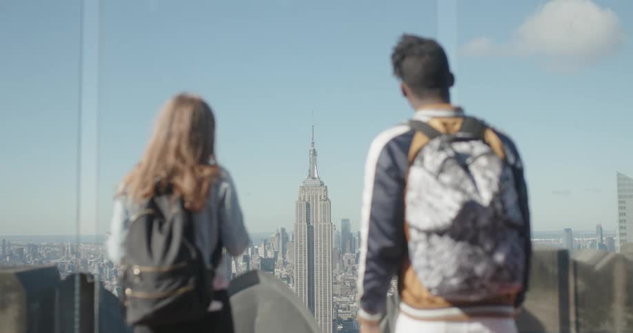 Two people are watching over the city from behind glass on the roof