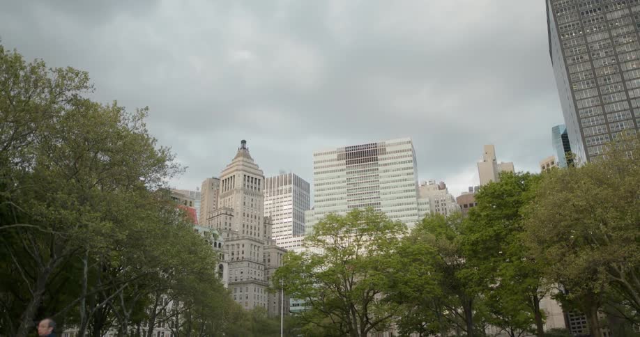 People walk past trees and city buildings
