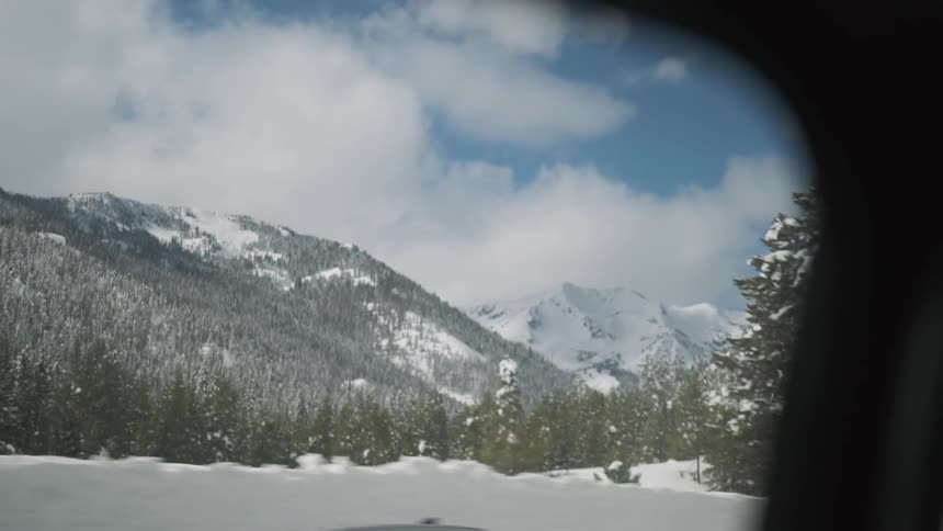 The mountain range is covered with snow as the cars drive by
