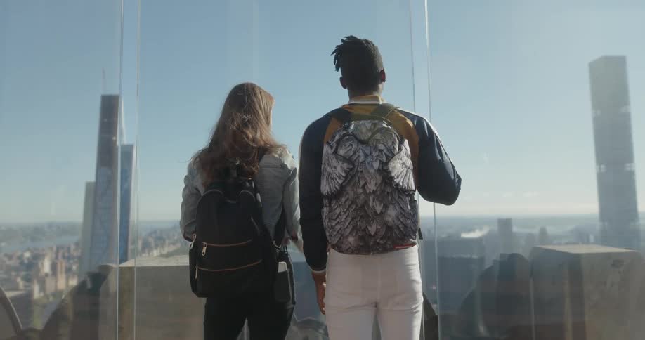 A man and woman stand by the glass looking out over the city