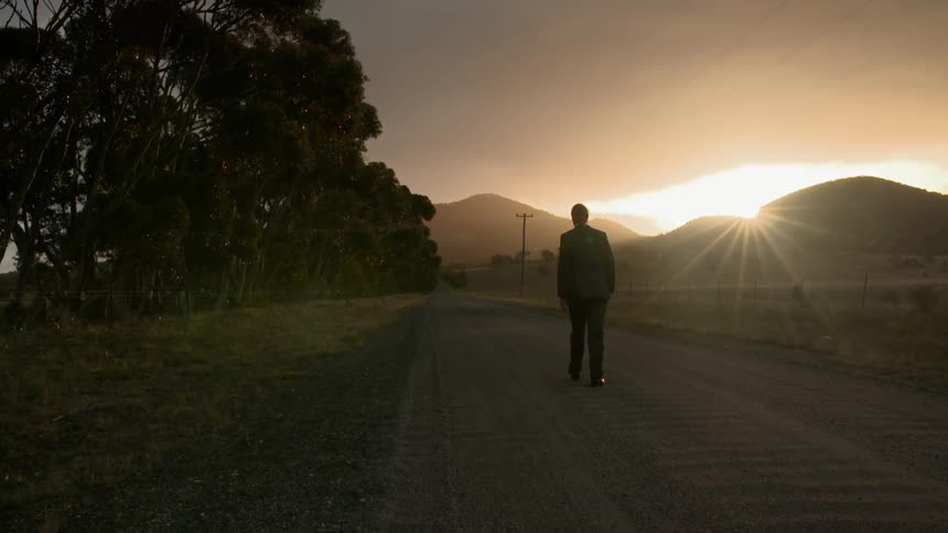 A man is walking down the road at sunset