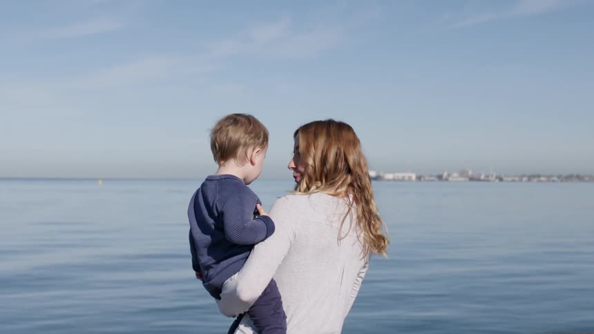 A woman holds a child near the shore