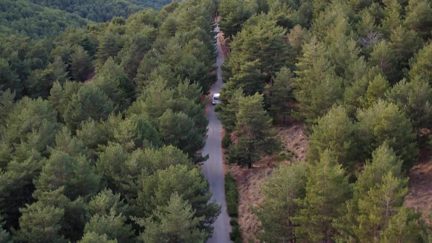 The white vehicle travels down the road on the cliff