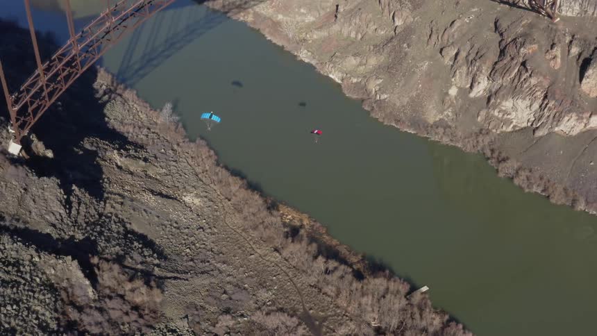 Vehicles travel over a bridge as two people parachute down